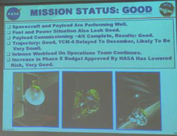 Image of slide projected on wall reading "Spacecraft and Payload Are Performing Well."